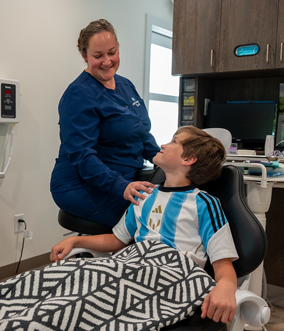 Little boy in dental chair smiling up at children's dentist in Stevensville